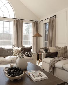 a living room filled with furniture and a large window covered in drapes, along with a bowl of rocks on the coffee table