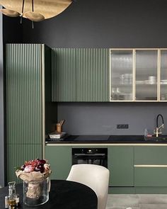 a kitchen with green cabinets and black counter tops, white chairs and a round dining table