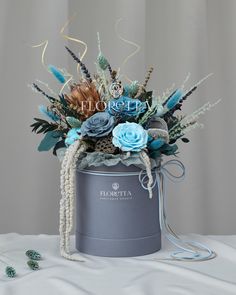 a blue flower arrangement in a gray bucket on a white tablecloth with beads and pearls