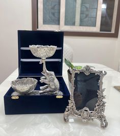 two silver items sitting on top of a table next to a vase and an empty box