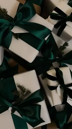 several white boxes with green bows and pine branches on them, all wrapped in satin ribbon