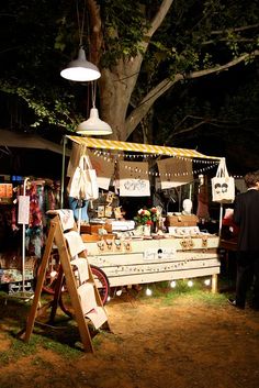 an outdoor market with people shopping and selling items at night time, in the background is a large tree