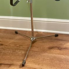 a metal tripod stands on a hard wood floor in front of a green wall