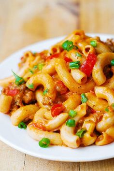 a white plate topped with macaroni and cheese covered in green onions on top of a wooden table