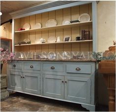 an old fashioned kitchen with blue cupboards and white dishes on the top shelf, next to a ladder