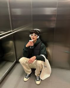 a man sitting on an elevator with headphones and a wine glass in his hand