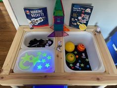 a wooden table topped with two trays filled with toys and books on top of it