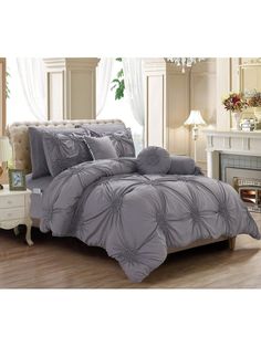 a bed with grey comforter and pillows on top of it in front of a fireplace