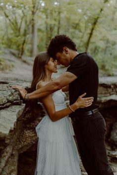 a man and woman standing next to each other in front of some rocks with trees behind them