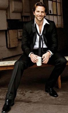 a man in a suit and tie sitting on a bench with a cup of coffee