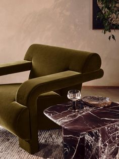 a green chair sitting on top of a marble coffee table next to a glass vase