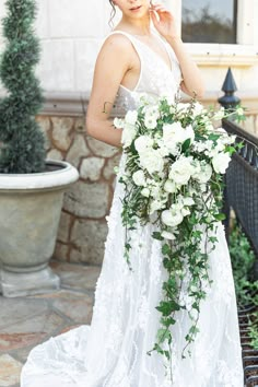 a woman in a white wedding dress holding a bouquet of flowers on her shoulder and looking at the camera