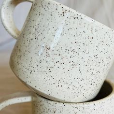 two white coffee mugs stacked on top of each other with speckled brown spots