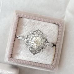 an engagement ring in a velvet box on a white cloth background with the diamond center surrounded by filigrees