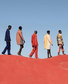 five men walking on top of a sand dune in the desert, wearing colorful clothing