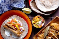 two plates with food on them sitting next to some breads and other foods in bowls