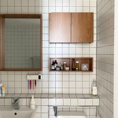 a bathroom with white tile and wooden cabinet above the sink is seen in this image