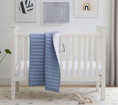 a white crib with blue blankets and pictures on the wall in front of it