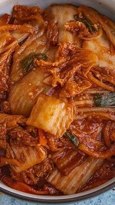 a pot filled with meat and vegetables on top of a blue tablecloth next to a wooden spoon