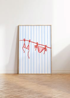 an art piece with clothes hanging on a line in front of a white wall and wooden floor