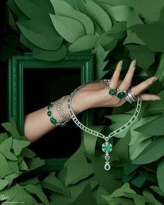 a woman's hand with green bracelets and rings on her wrist, surrounded by leaves