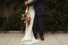 a bride and groom standing next to each other in front of a bush holding an umbrella