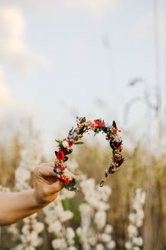 a person holding up a flowered headband in front of some trees and bushes