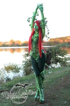 a woman dressed in green and red is standing by the water with her hands up