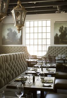 an empty restaurant with many tables and chairs in front of the window, along with two chandeliers hanging from the ceiling