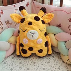 a crocheted giraffe pillow sitting on top of a bed next to pillows