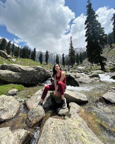 a woman sitting on top of a rock next to a river