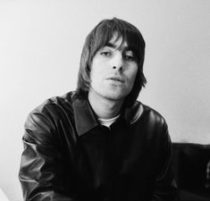 a black and white photo of a man in a leather jacket sitting at a piano