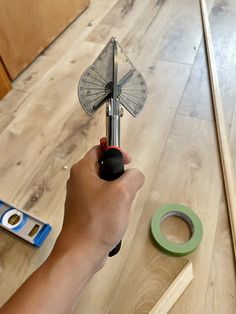 a person holding a small metal object on top of a wooden floor next to tape