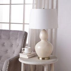 a white lamp sitting on top of a table next to a gray chair and window