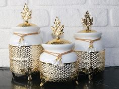 three white and gold canisters sitting next to each other on a black table