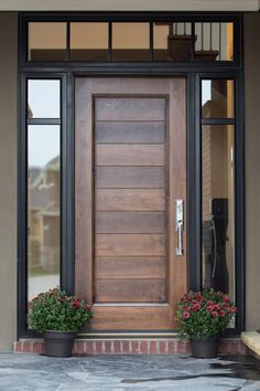 a wooden door with two planters on the side and glass windows above it, in front of a house