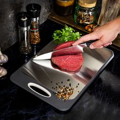 a person cutting up meat on top of a metal tray next to vegetables and spices