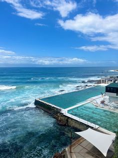 an outdoor swimming pool next to the ocean under a blue sky with wispy clouds