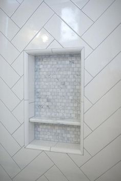 a white bathroom with herringbone tile on the wall and shelves in the corner,