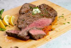 a piece of steak on a cutting board with lemon wedges