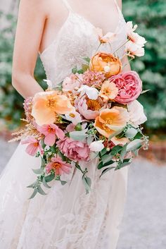 a woman holding a bouquet of flowers in her hand and wearing a wedding dress with lace