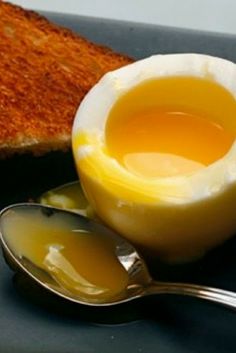 an egg yolk in a bowl next to a spoon and slice of toast on a plate