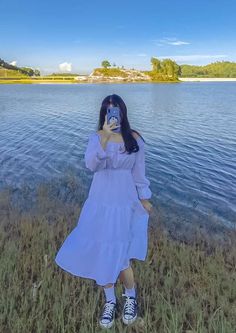 a woman taking a photo with her cell phone in front of a body of water