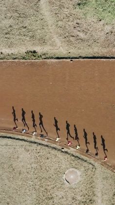 a group of people running down a dirt road in the middle of an open field