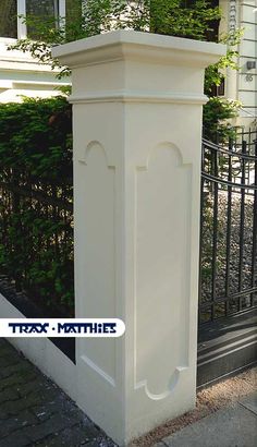 a tall white planter sitting on the side of a sidewalk next to a fence