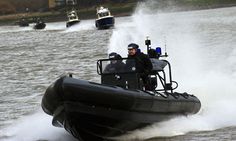 two police officers riding in a speedboat on the water with other boats behind them