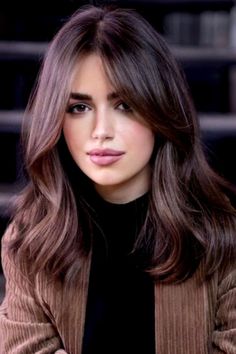 a woman with long brown hair sitting in front of some stairs and looking at the camera