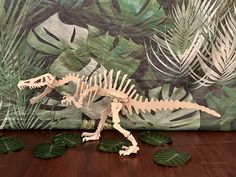 a toy t - rex standing on top of a wooden floor next to green leaves