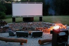 a fire pit with chairs around it and a movie screen in the background