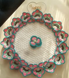 a crocheted doily with pink and blue flowers on it sitting on a table